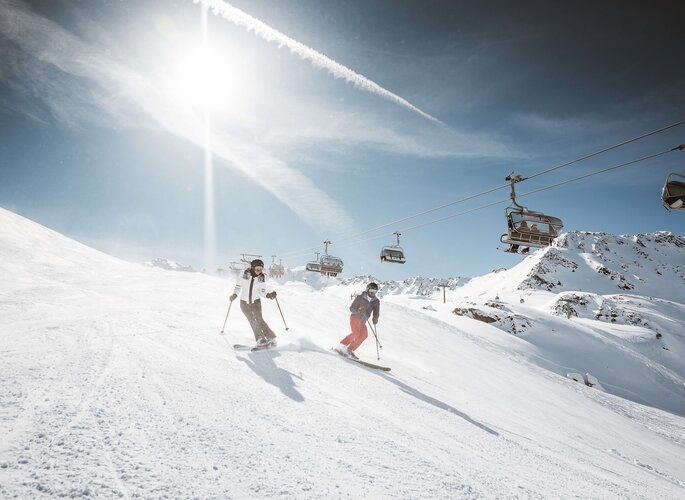 Skiurlaub an der Piste in Obergurgl Zwei Skifahrer fahren auf einer sonnigen Skipiste unter einem Sessellift ab.