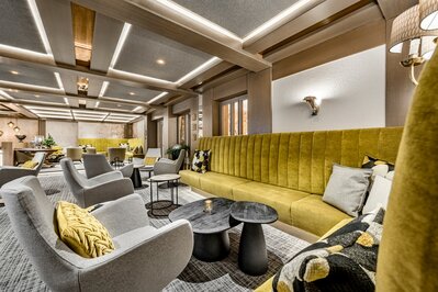 Eine stilvolle Lounge mit Polstersesseln, gelber Sitzbank und warmem Licht im Hotel Jenewein.