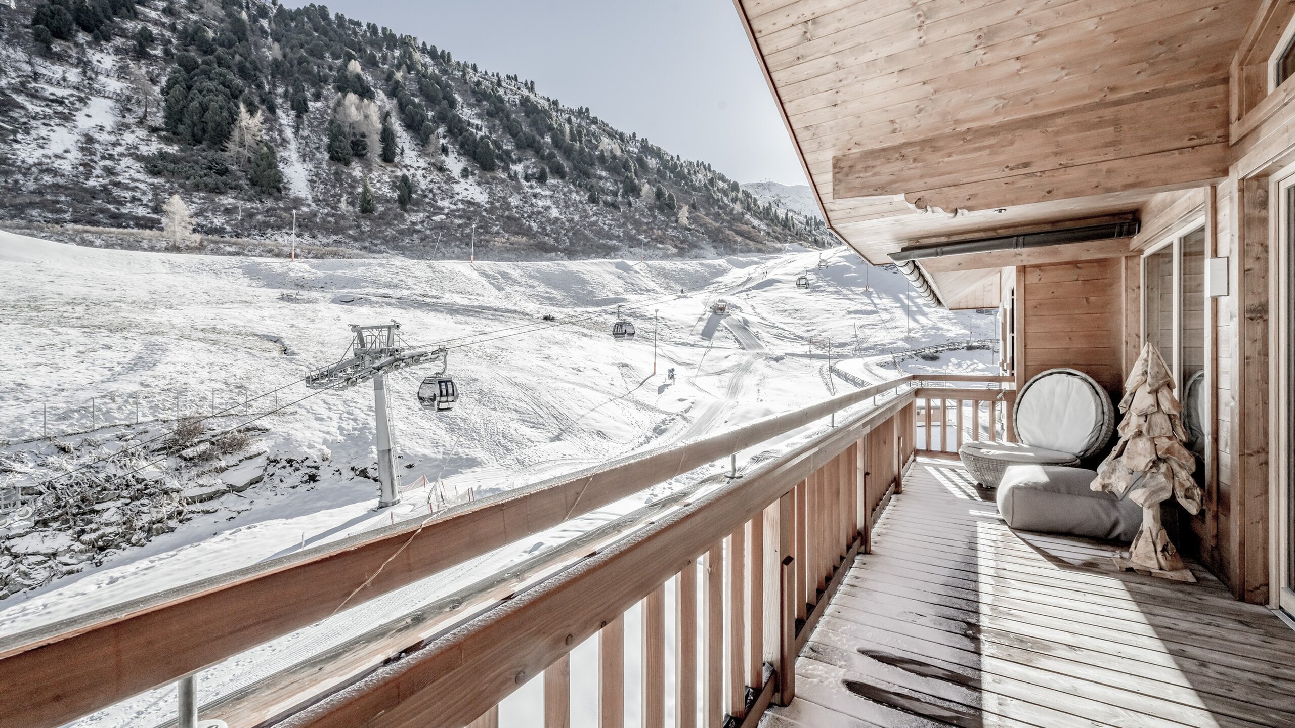 Ein Holzbalkon mit Blick auf die verschneite Berglandschaft und die Seilbahntrasse in Obergurgl.