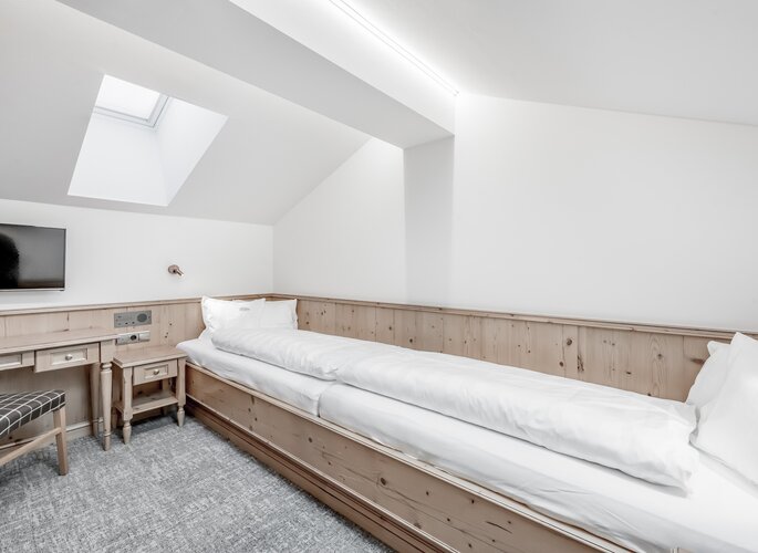 Ein helles Maisonettenzimmer mit Einzelbett, Dachfenster und Holzverkleidung im Hotel Jenewein.