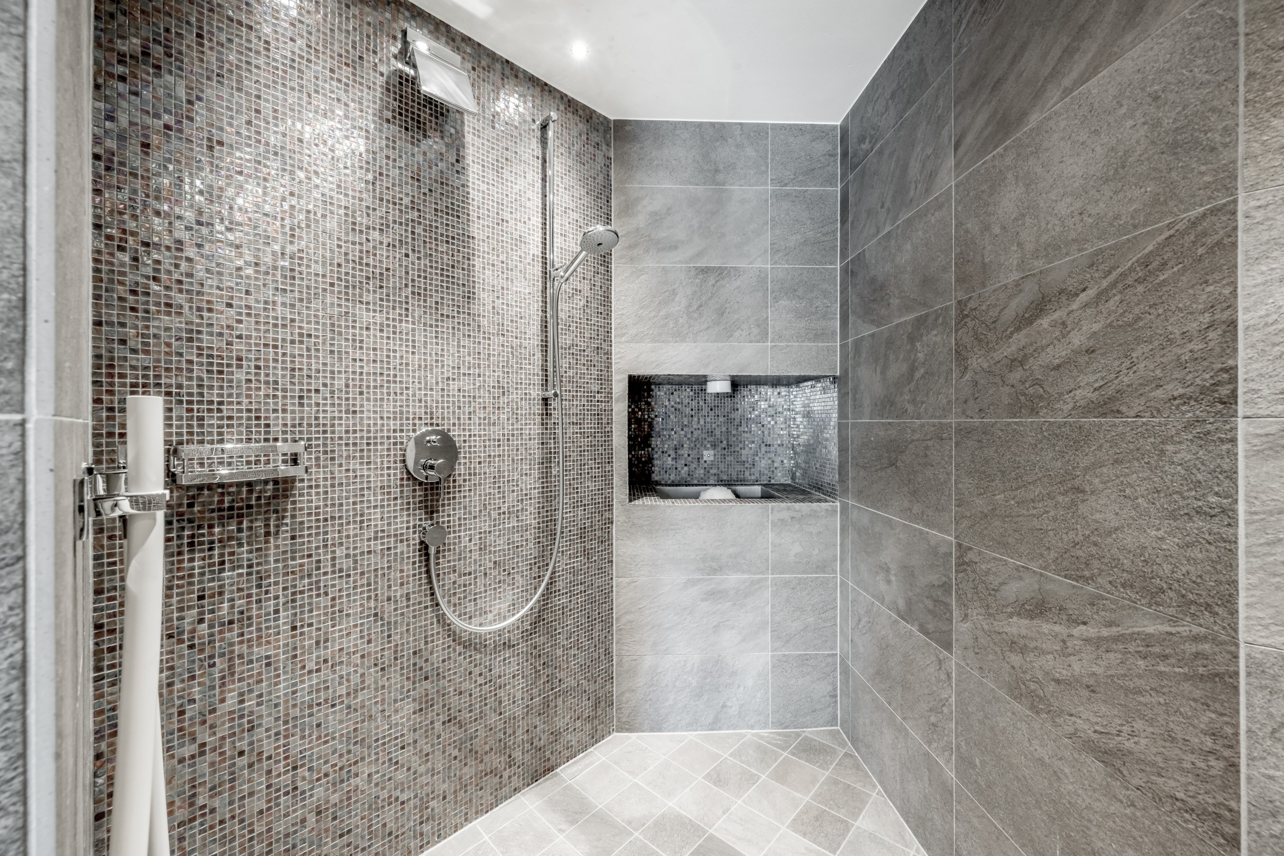 Eine moderne Dusche mit Mosaik- und Natursteinfliesen im Wellnessbereich.