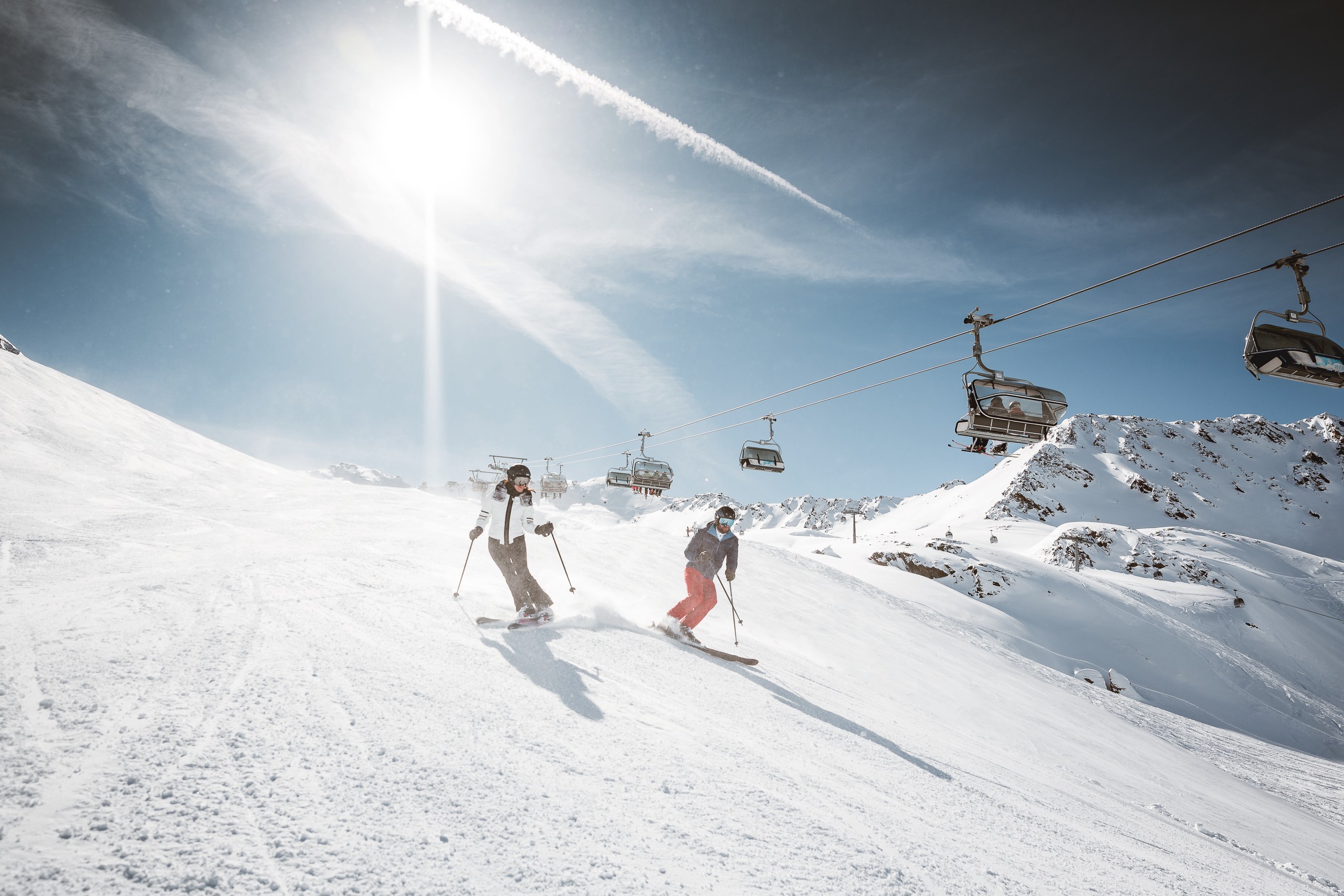 Skiurlaub an der Piste in Obergurgl Zwei Skifahrer fahren auf einer sonnigen Skipiste unter einem Sessellift ab.